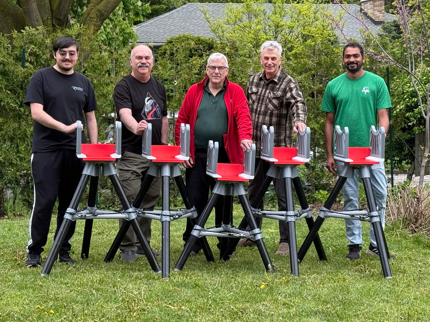 Five Hamilton Centre RASC volunteers standing behind five finished telescope tripods on a lawn